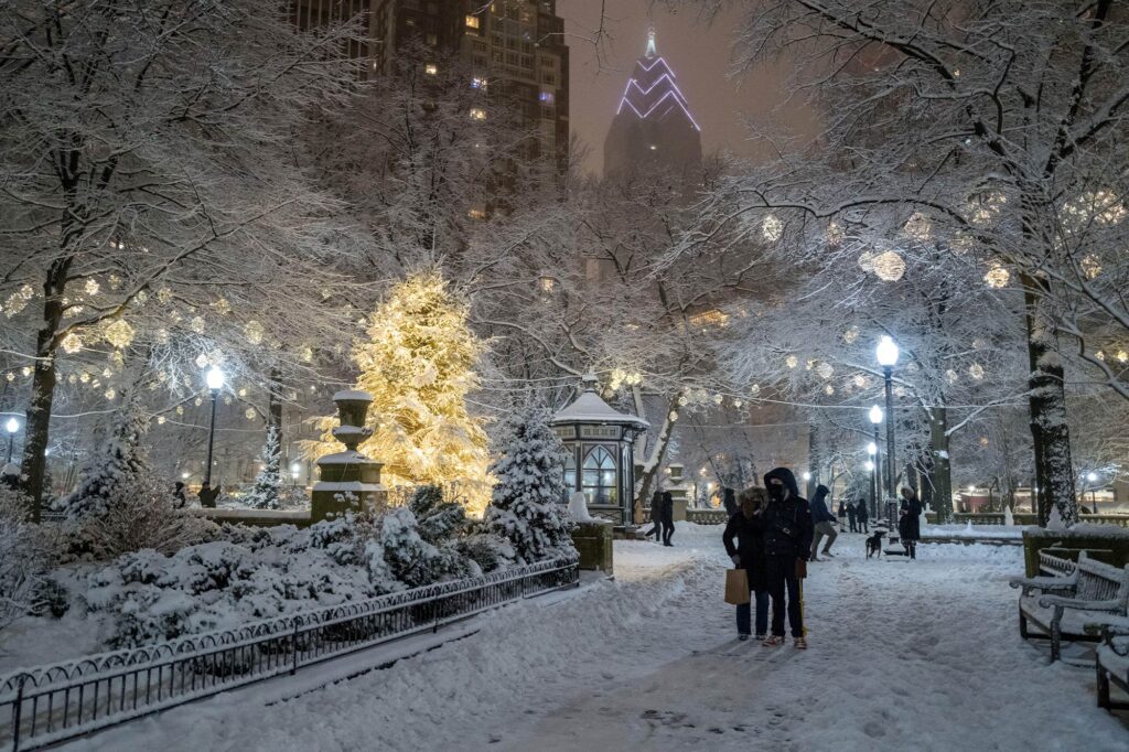 Rittenhouse Square Park at night with snow covered paths, illuminated trees, lit gazebo, and tall buildings behind.