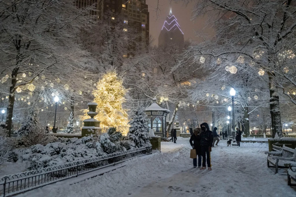 Rittenhouse Square Park at night with snow covered paths, illuminated trees, lit gazebo, and tall buildings behind.